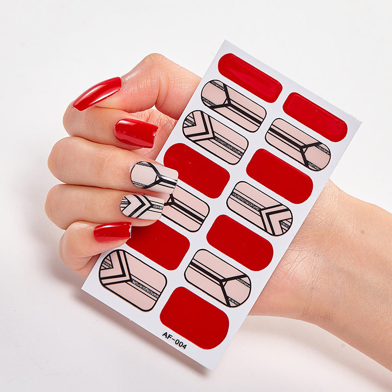 Red nail polish on a hand holding a nail art sticker sheet featuring geometric designs and red accents.