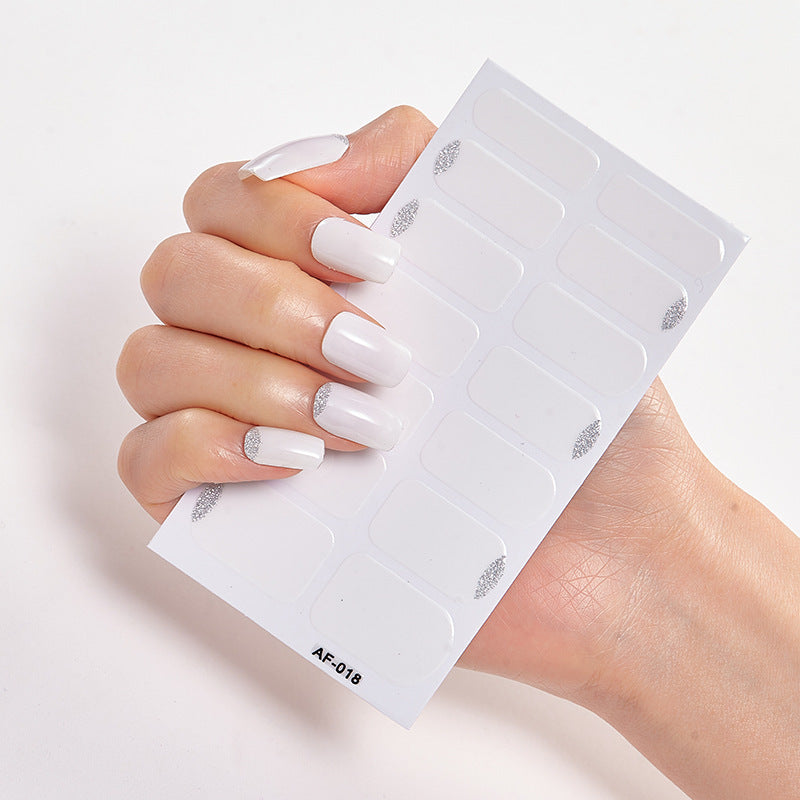 White nail tips with silver accents held in a hand, alongside a sheet of nail stickers for decoration.