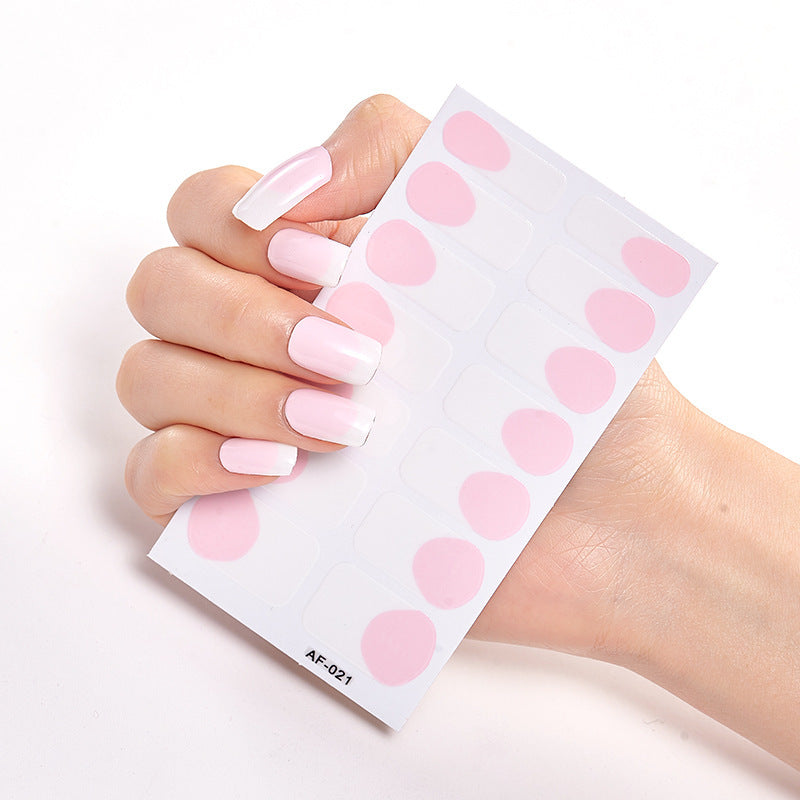 Long, manicured nails in a gradient pink and white design hold a sheet of circular pink nail stickers.