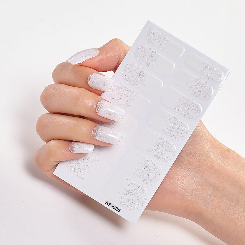 Hand holding a sheet of nail stickers featuring white glittery designs on a clear background.