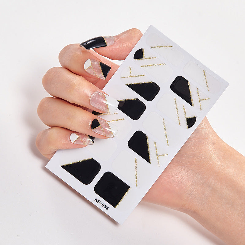 Nail art design featuring black, white, and gold geometric patterns on a clear background with a hand holding the nail sti...