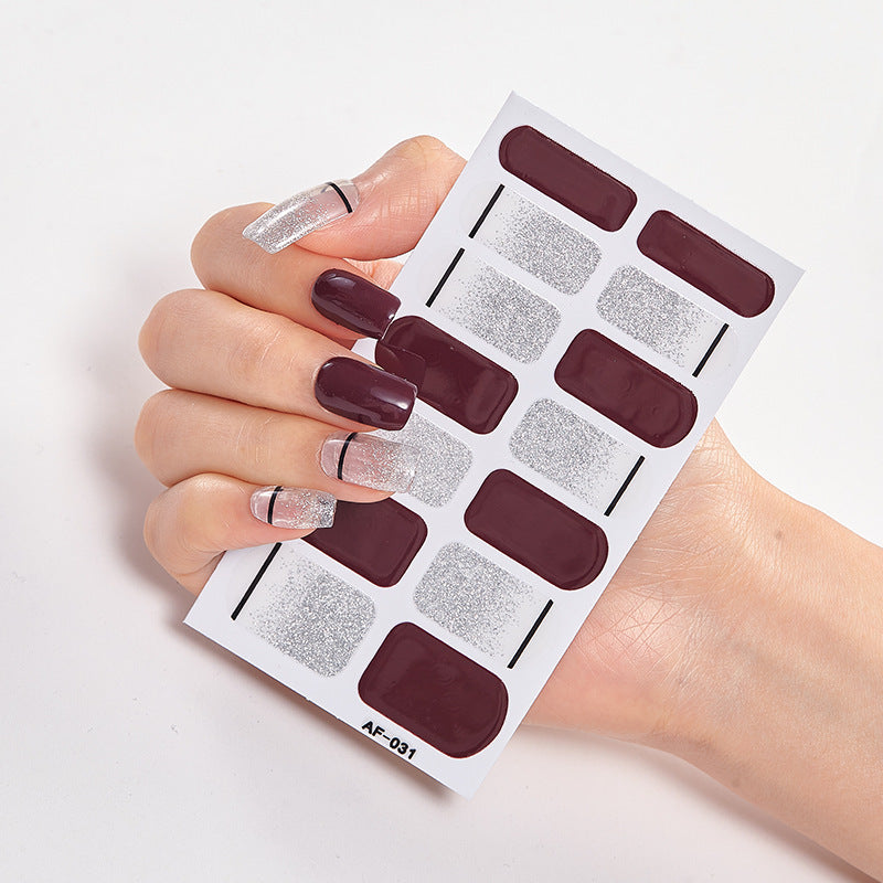 Hand holding a nail art sticker sheet featuring dark burgundy and silver glitter designs.