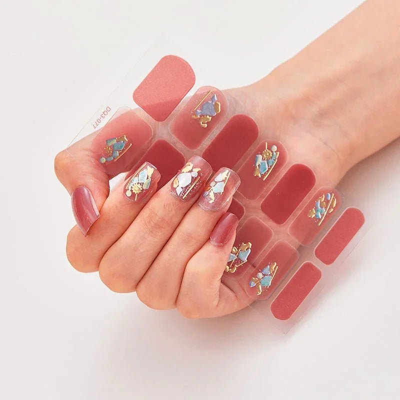 Currant™ nail wraps displayed on a hand, featuring pink, blue, and gold designs on clear stickers.