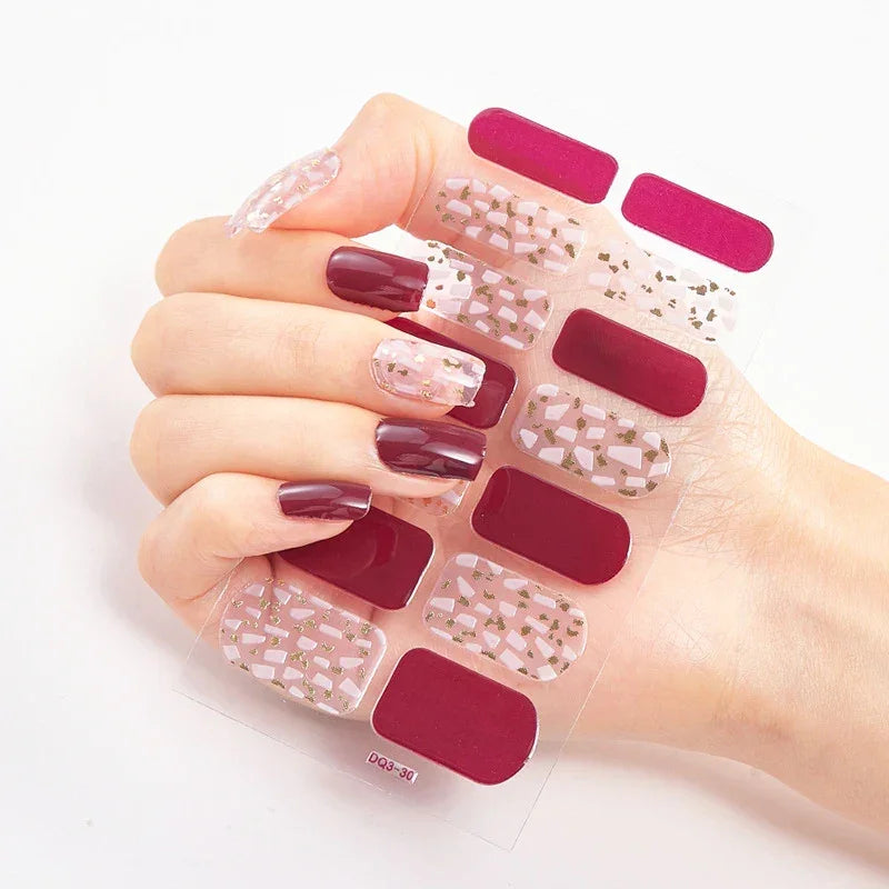 Currant™ nail wraps in burgundy, clear, and gold designs displayed in a hand with manicured nails.