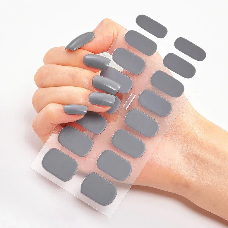 Currant™ nail wraps in gray held by a hand with long gray nails, showcasing a sheet of matching nail stickers.