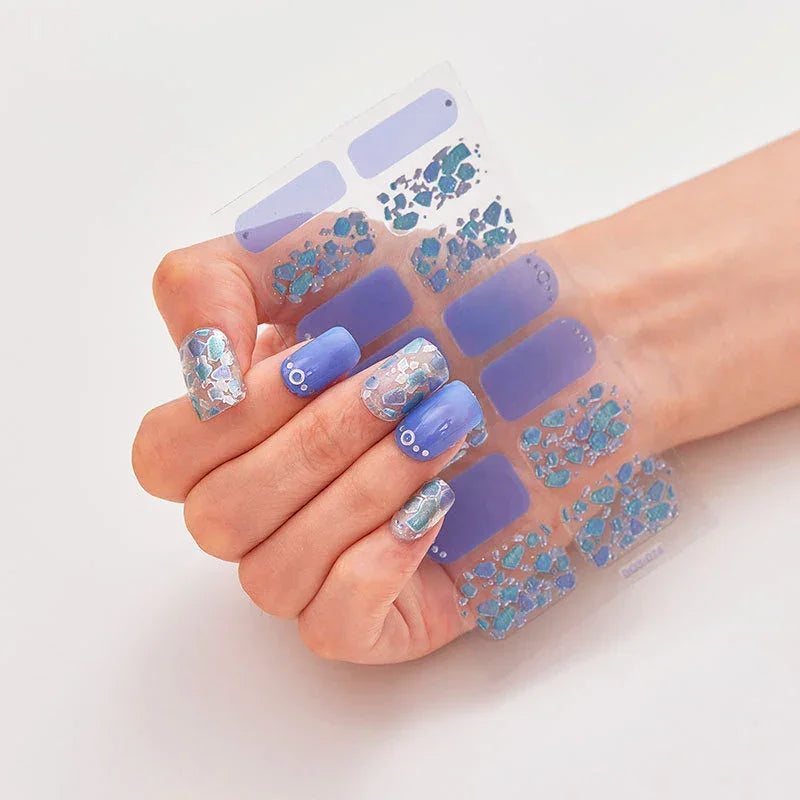 Currant nail wraps in a hand, showcasing blue and silver designs with floral and geometric patterns.