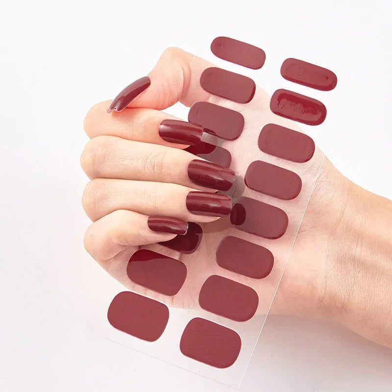 Currant™ nail wraps in dark red, featuring various shapes, held in a hand with long, polished nails.
