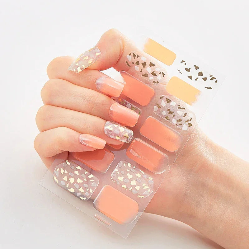 Currant™ Marble press-on nails in peach and gold with various designs on a clear backing held by a hand.