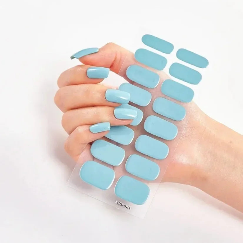 Hand holding blue Currant™ nail wraps on clear backing, featuring various sizes and shapes of press-on nails.