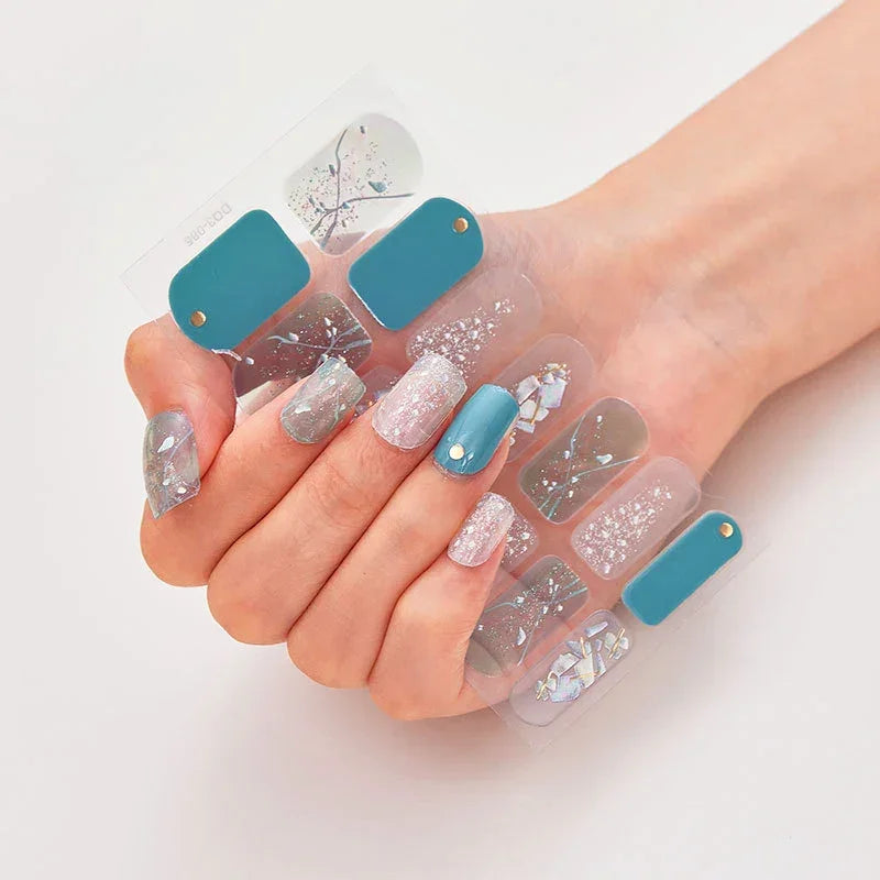 Currant™ nail wraps on a hand, showcasing teal, glitter, and various intricate designs.