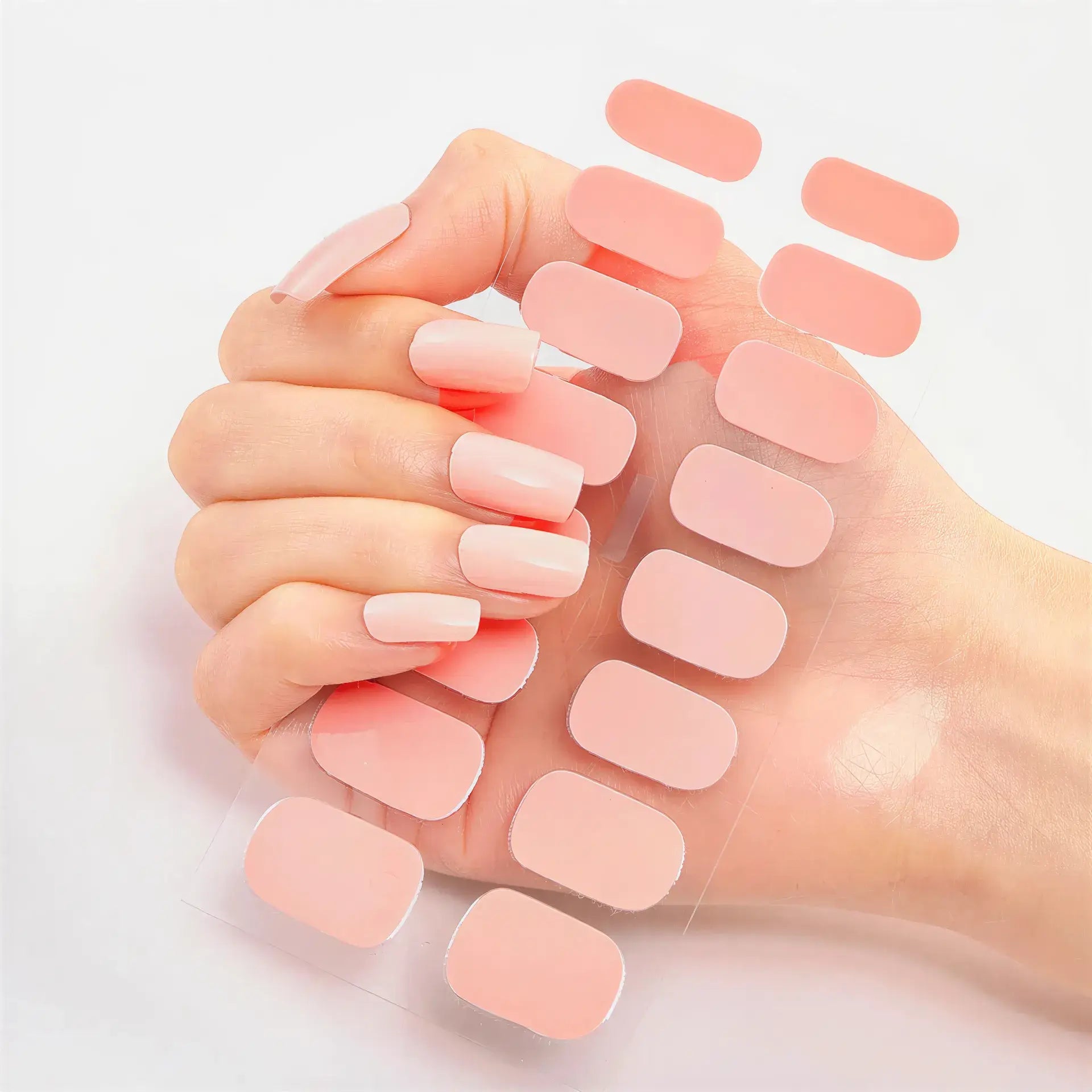 Hand displaying light pink press-on nails while holding a sheet of matching light pink nail wraps.