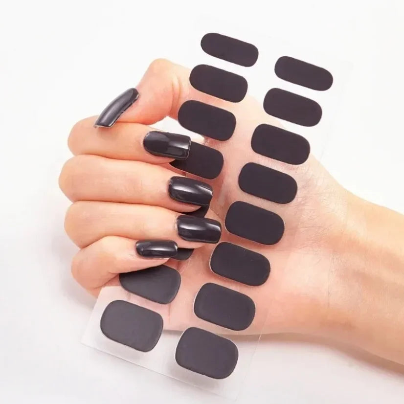 Currant™ nail wraps in a hand with long, glossy black nails holding a sheet of black nail wraps.