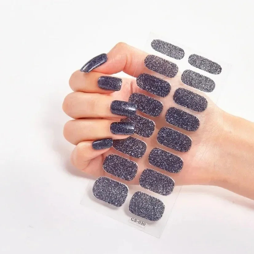Currant™ Star nail wraps in dark blue with glitter, displayed on a hand holding a sheet of various nail designs.