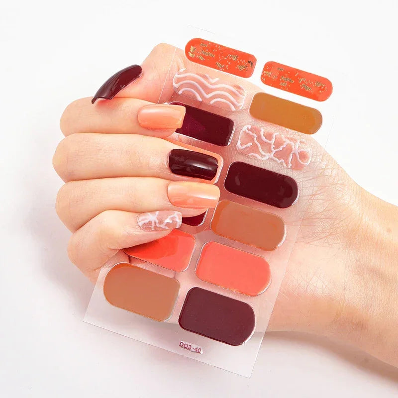 Currant nail wraps on a hand, showcasing shades of orange, red, brown, and intricate decorative patterns.