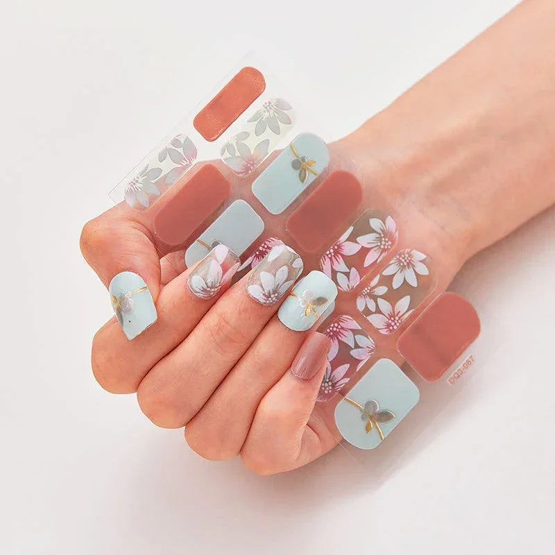 Currant™ nail wraps with floral designs in blue, pink, and beige displayed on a manicured hand against a light background.