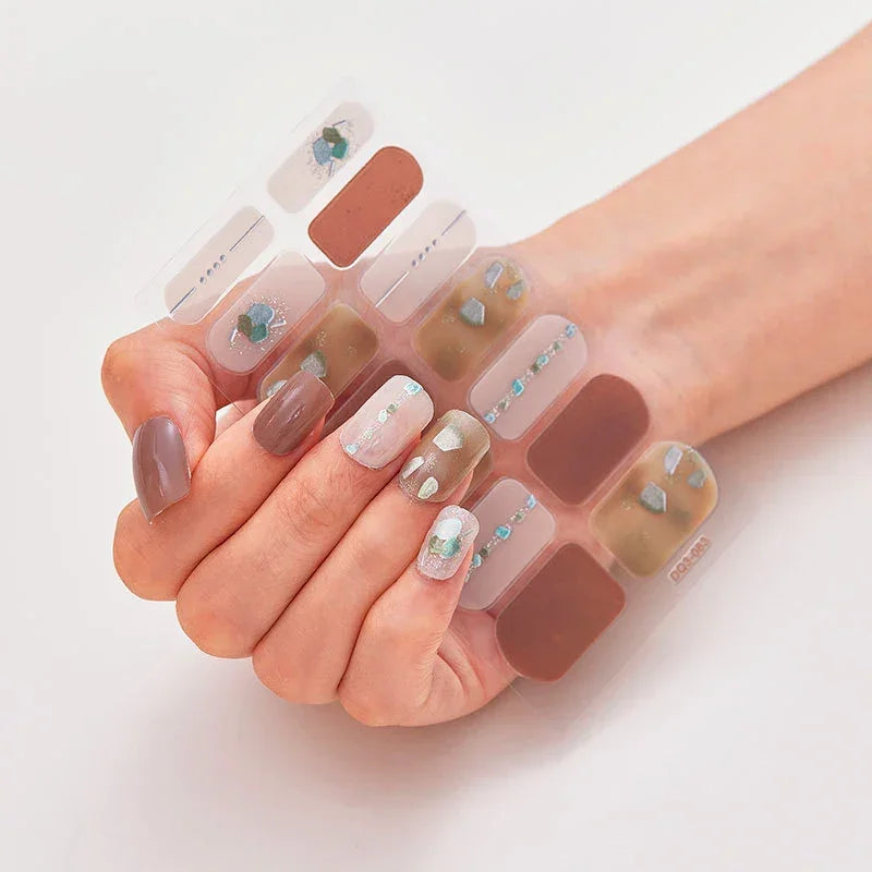Currant™ nail wraps on a hand, showcasing various designs in brown, pastel colors, and embellishments.
