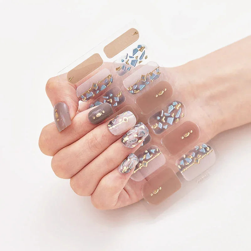 Currant™ nail wraps featuring neutral marble designs and gem accents on a hand holding a display sheet of press-on nails.