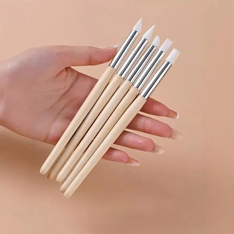 Set of five application wands with white tips and wooden handles, held in a hand against a beige background.